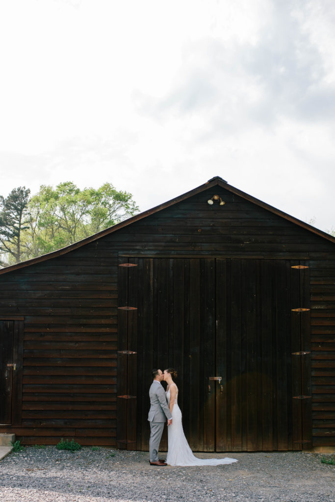 Bride and groom kissing in front of barn