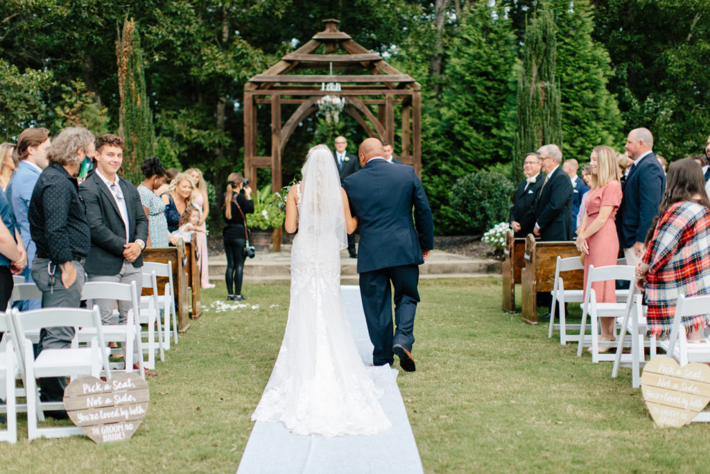 Father, in blue suit, walking his daughter, in white dress, down the aisle at Rolling Hill Farms in Monroe NC.
