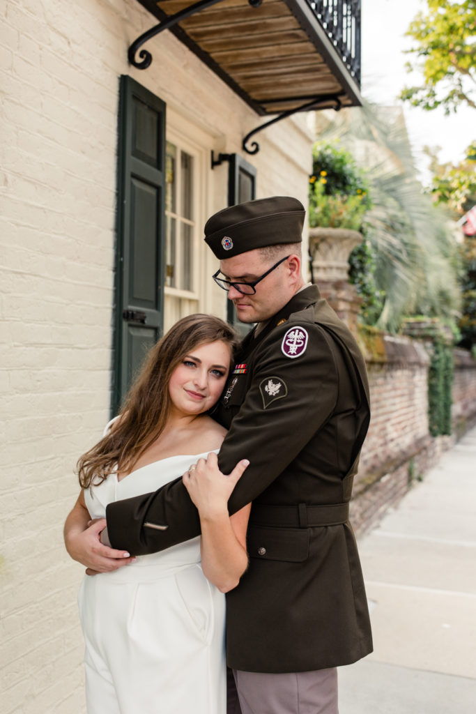 Groom, wearing military uniform, hugging his bride, in a white jump suit in Charleston South Carolina.