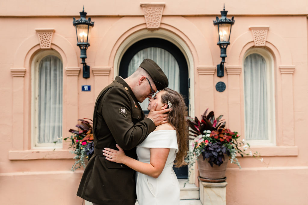 Groom, wearing military uniform, hugging his bride, in a white jump suit in Charleston.