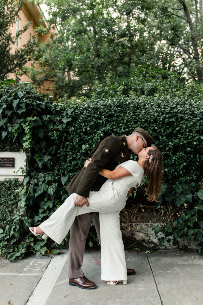Groom, wearing military uniform, kissing his bride, in a white jump suit in Charleston.