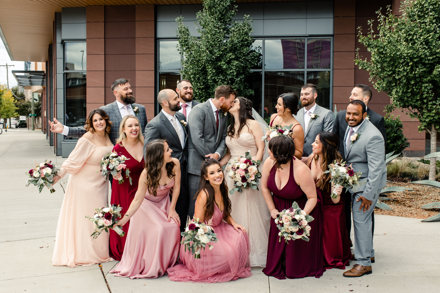 Groomsmen in grey suits and bridesmaids in pink dresses cheer on the bride in groom at the Collector's Room Charlotte wedding venue. Photographed by Charlotte wedding photographer.