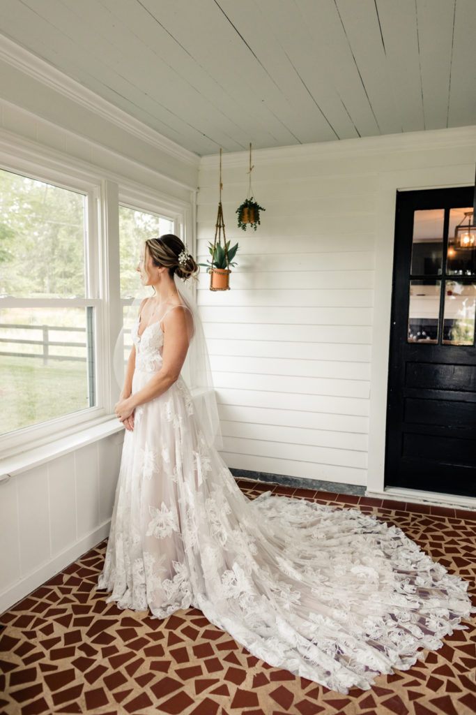 Bride in long white laced dress looking out window at Bansen Farms wedding venue in Charlotte NC.