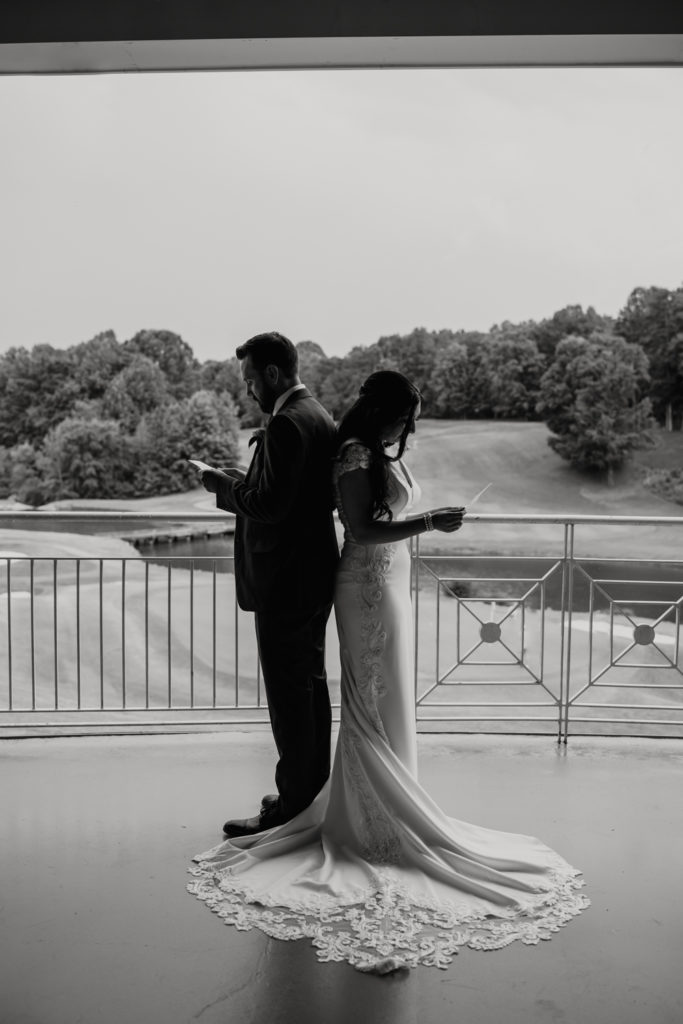 Bride in white dress back to back with groom in black suit reading each other letters on wedding day at Northstone Country Club in Charlotte. Photographed by Charlotte wedding photographer.