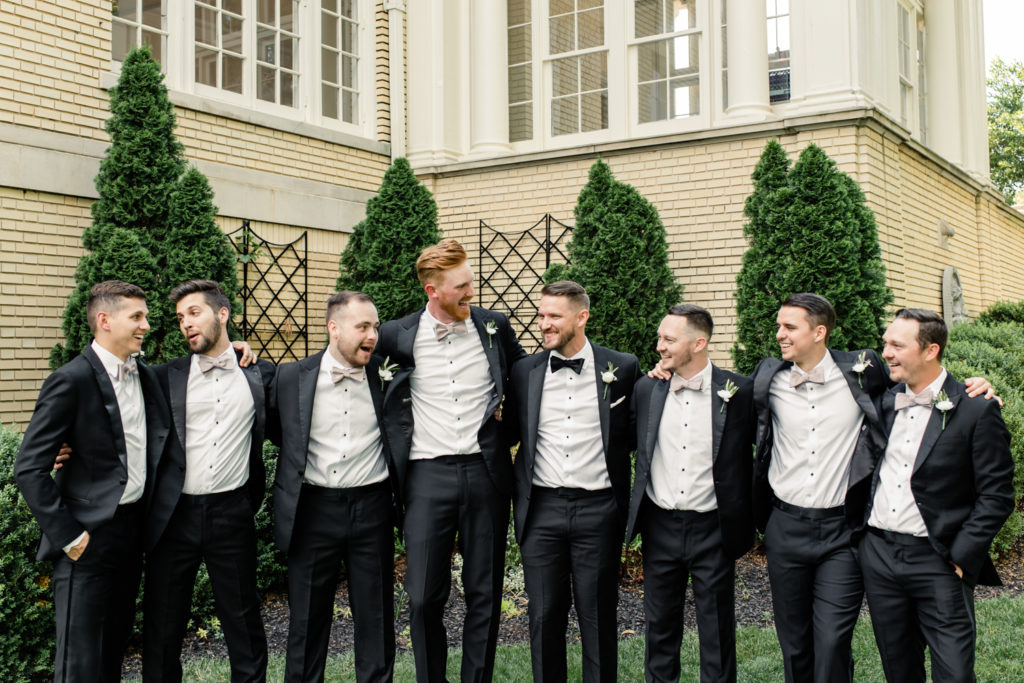 Groom and seven groomsmen in black suits hugging each other laughing at SePark Mansion Gastonia Wedding Venue. Photographed by Charlotte wedding photographer.
