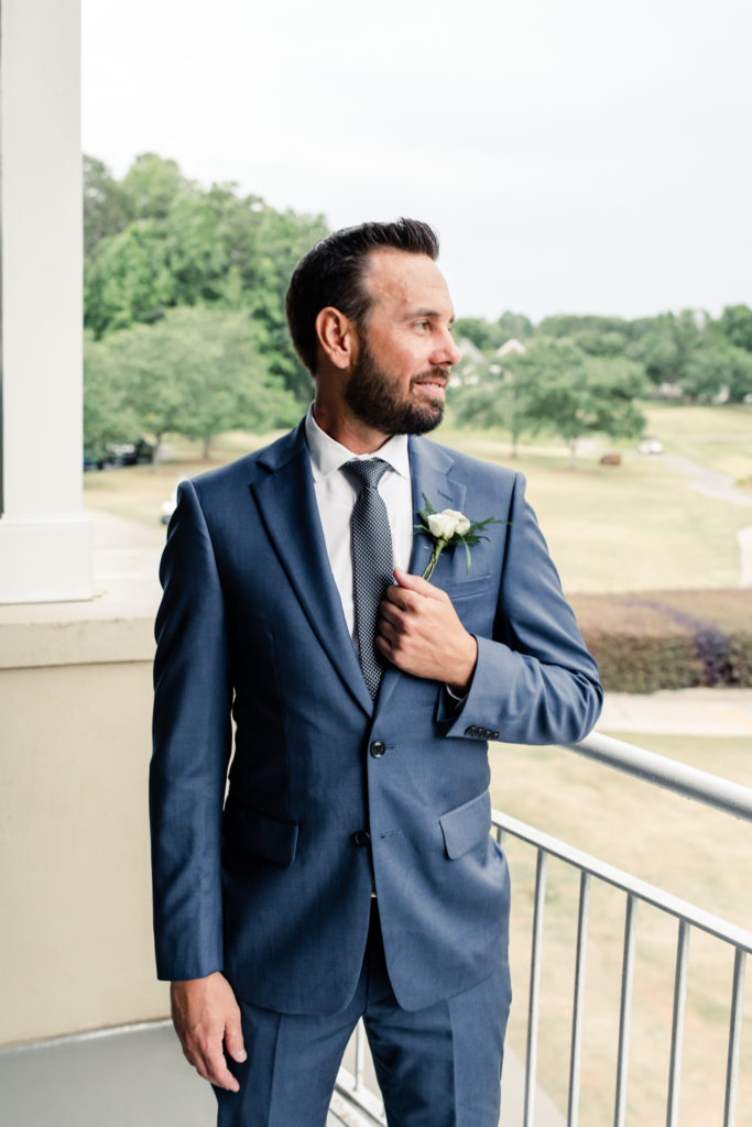 Groom with brown hair in blue suit and tie has a white boutonnière at Northstone Country Club in Charlotte. Photographed by Charlotte wedding photographer.