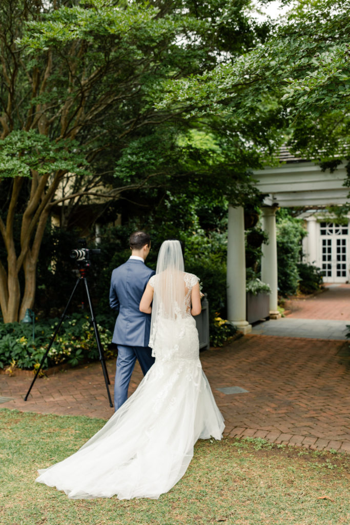 Bride in white lace dress and pink and white bouquet walking holding hands with groom in blue suit at Daniel Stowe Botanical wedding venue. Photographed by Charlotte wedding photography.