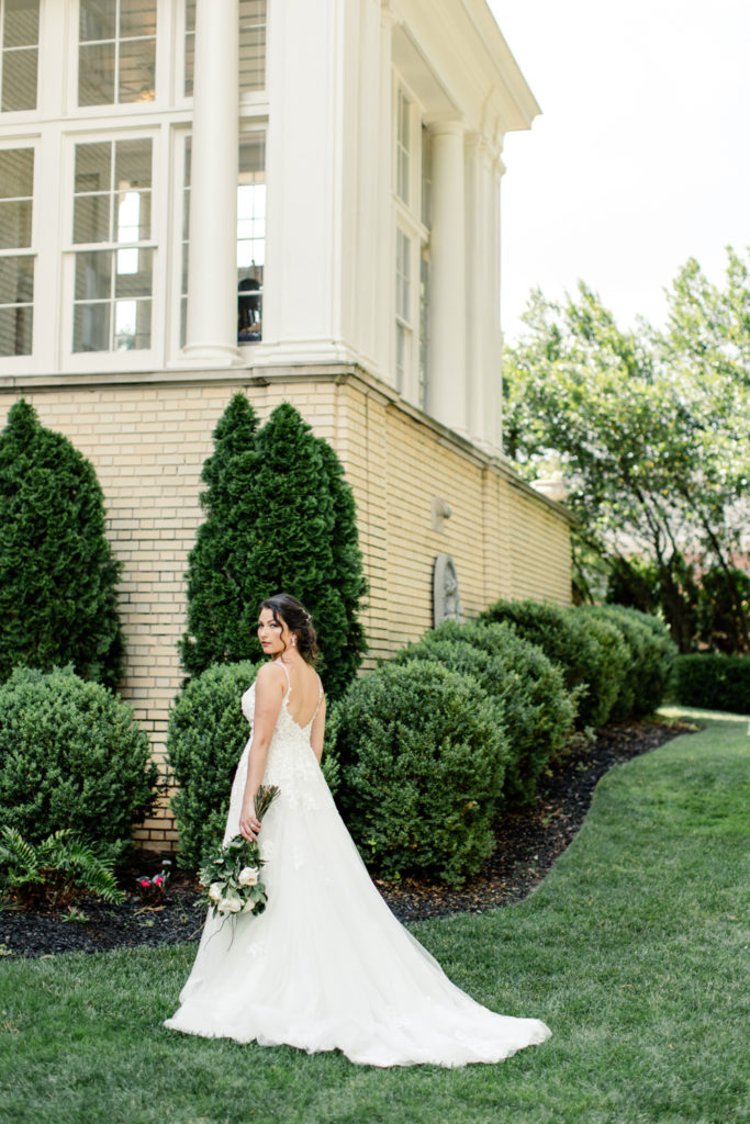 Bride in white lace dress standing with green and white bouquet looking over her left shoulder at SePark Mansion Gastonia Wedding Venue. Photographed by Charlotte wedding photographer.