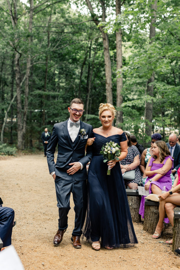 Groom, in navy suit, walking down aisle with sister, in navy dress, at Carolina Country weddings venue in Charlotte.