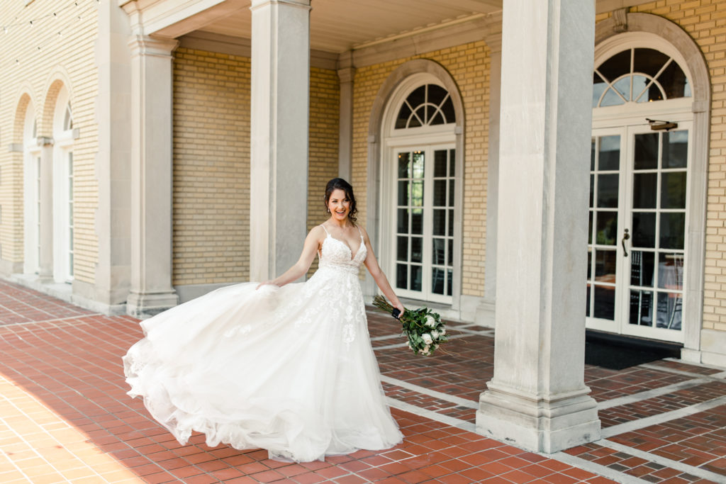 Bride in white lace dress holding green and white bouquet playing with the train of her dress at SePark Mansion Gastonia Wedding Venue. Photographed by Charlotte wedding photographer.