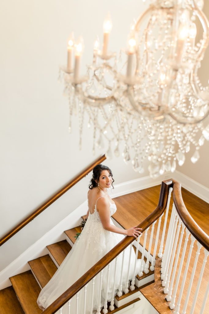 Bride in white lace dress walking up a brown and white staircase holding the railing at SePark Mansion Gastonia Wedding Venue. Photographed by Charlotte wedding photographer.