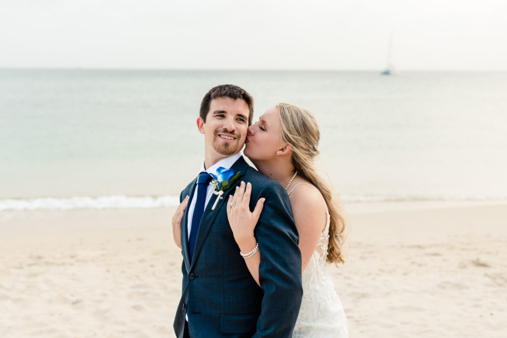 Bride, in white dress, kissing groom, in blue suit, on the beach at the St. Lucia Grande Sandals Resort. Photographed by Charlotte wedding photographer.