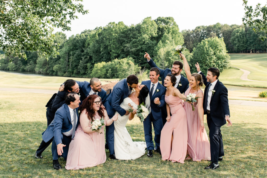 Bride and groom kiss while wedding party cheers them on at Northstone Country Club in Charlotte. Photographed by Charlotte wedding photographer.