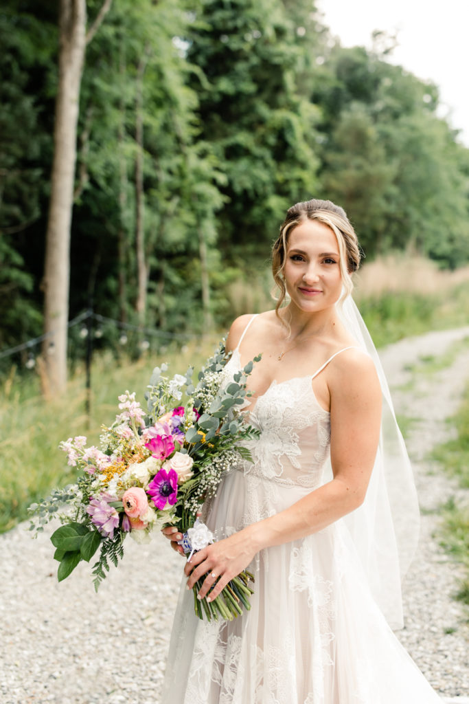 Bride wearing white lace dress holds her pink, purple, white and green bouquet at Bansen Farms wedding venue in Charlotte NC.