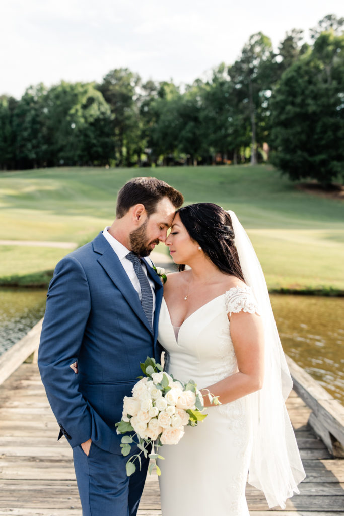 Bride, in white gown and veil, nose to nose with groom, in blue suit and tie on a golf course at Northstone Country Club in Charlotte. Photographed by Charlotte wedding photographer.
