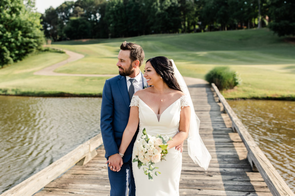 Bride in white laced dress and white veil holds hands with groom in blue suit and tie smiling on the golf course at Northstone Country Club in Charlotte. Photographed by Charlotte wedding photographer.