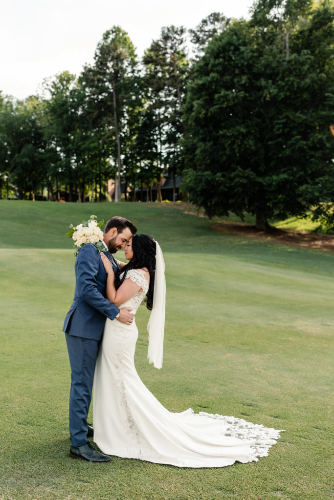 Bride in white wedding dress and veil nose to nose with groom in blue suit on golf course at Northstone Country Club in Charlotte. Photographed by Charlotte wedding photographer.