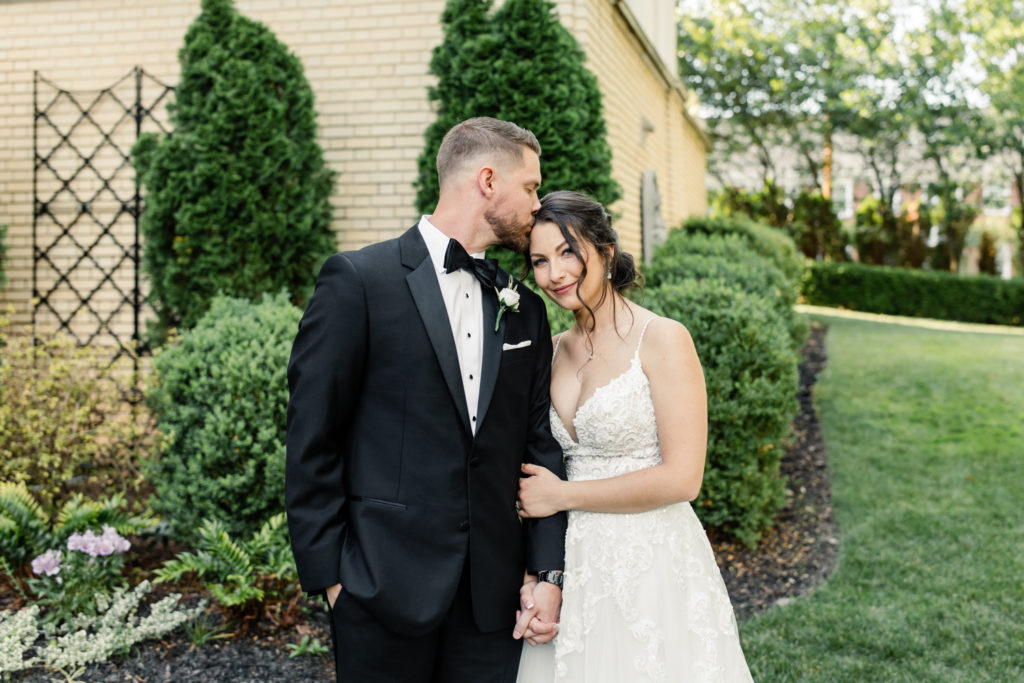 Groom in black suit and bowtie kissing the brides forehead at SePark Mansion Gastonia Wedding Venue. Photographed by Charlotte wedding photographer.