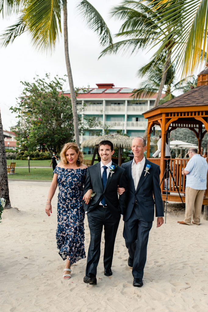Groom walks down beach ceremony aisle with mom and dad at the St. Lucia Grande Sandals Resort. Photographed by Charlotte wedding photographer.