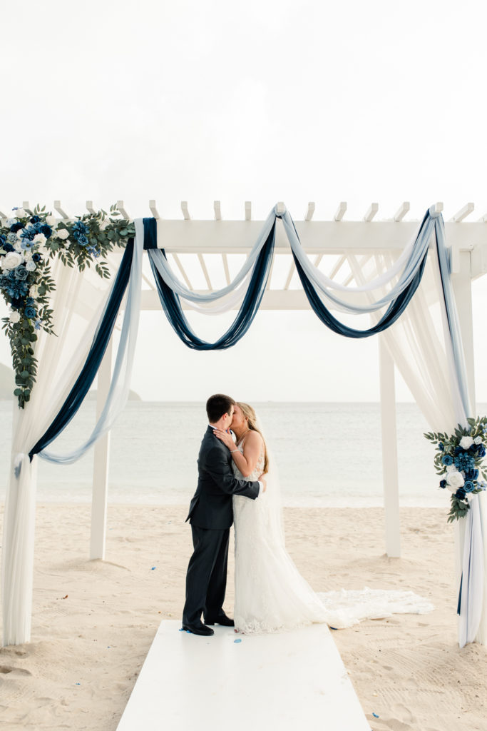 Bride and groom kissing for the first time on the beach during ceremony at the St. Lucia Grande Sandals Resort. Photographed by Charlotte wedding photographer.