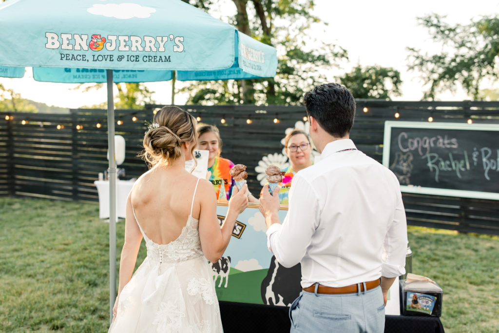 Bride in white dress eating Ben and Jerry's ice cream with groom in white shirt during their wedding at Bansen Farms wedding venue in Charlotte NC.