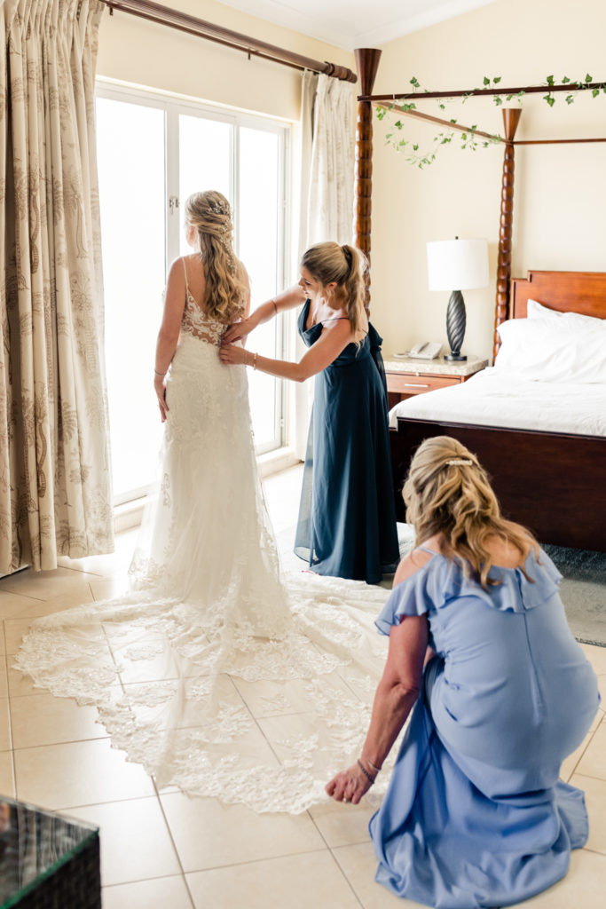 Bride, in white lace dress, getting ready with mother and sister in the hotel at the St. Lucia Grande Sandals Resort. Photographed by Charlotte wedding photographer.