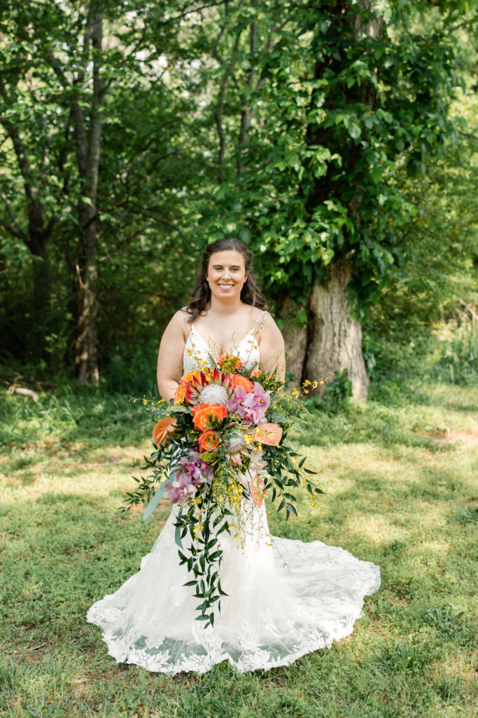 Bride in white lace dress holding a giant bouquet of orange, purple and green flowers 1932 Barn Wedding Venue in Charlotte

