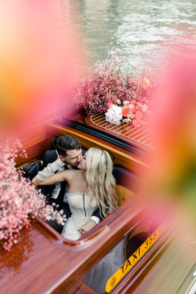 Bride and groom kissing in water taxi decorated in pink flowers in Venice Italy. Photographed by Charlotte wedding photographer.