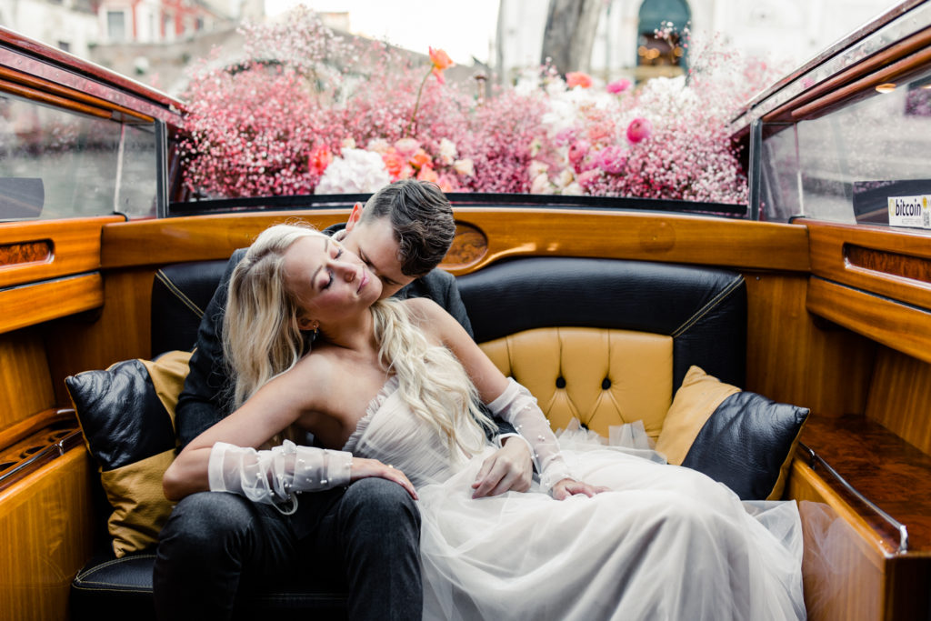 Groom kissing the cheek of bride in water taxi decorated in pink flowers in Venice Italy. Photographed by Charlotte wedding photographer.