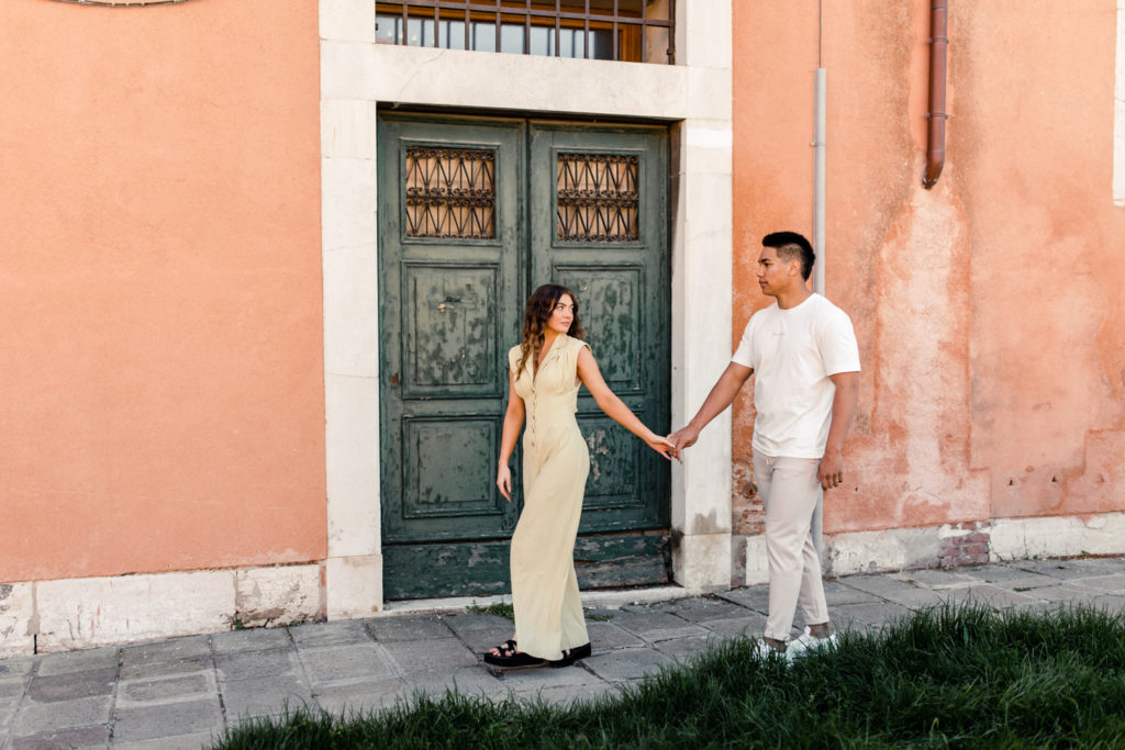 Boy, in white shirt, holding hands and walking with girl, in yellow jumpsuit, in Venice Italy. Photographed by Charlotte wedding photographer.