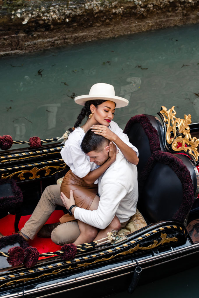 Girl, in brown leather dress and white button down, sitting in a gondola with boy, in white shirt, in Venice Italy. Photographed by Charlotte wedding photographer.