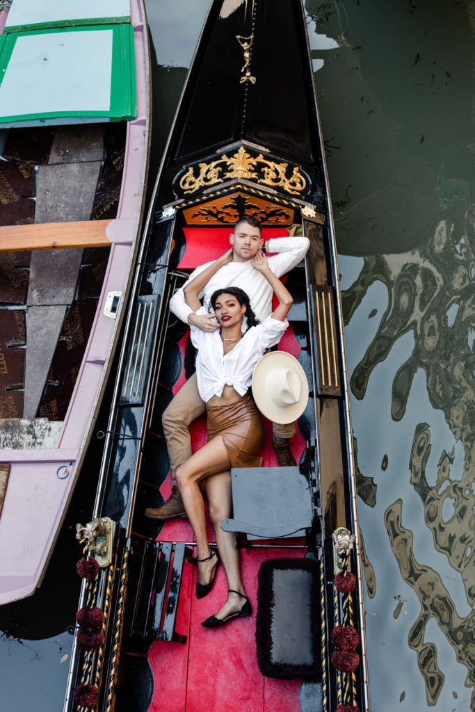 Girl, in brown leather dress and white button down, laying in a gondola with boy, in white shirt, in Venice Italy. Photographed by Charlotte wedding photographer.