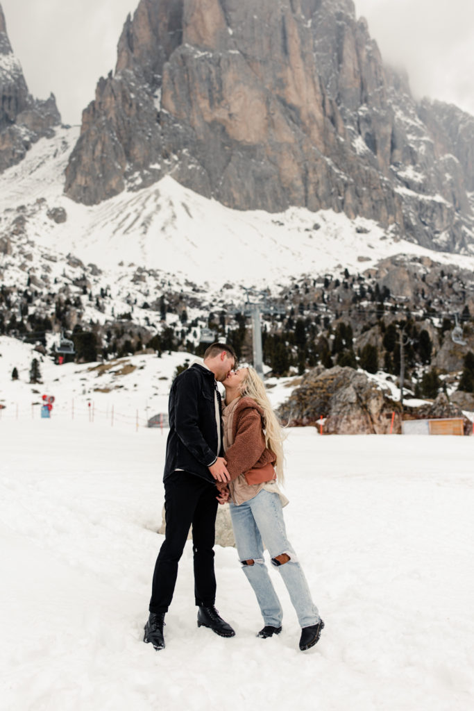 Boy and girl kissing on top of a snowy mountain in Dolomites Italy. Photographed by Charlotte wedding photographer.