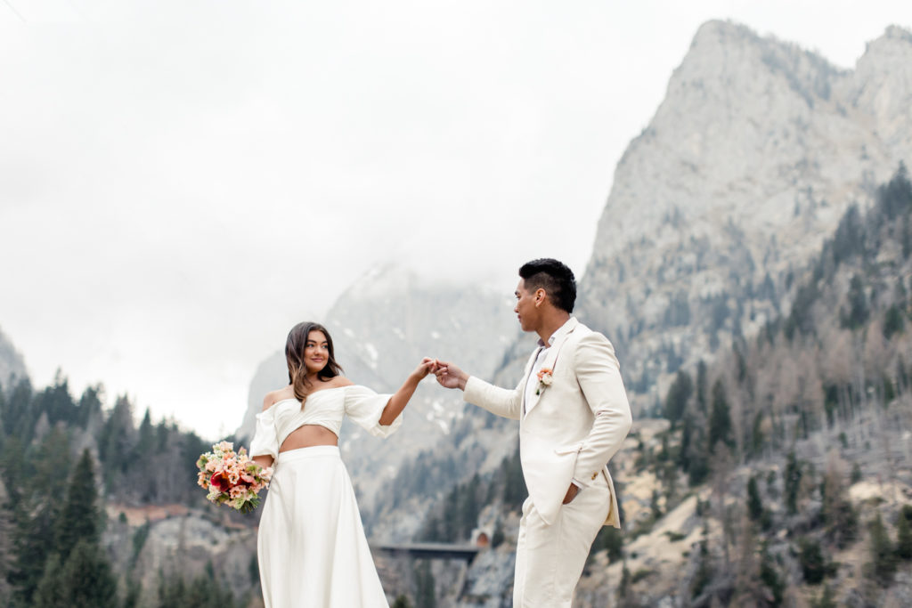 Groom, in cream suit, dancing with bride, in white dress holding pink bouquet in Dolomites Italy. Photographed by Charlotte Wedding Photographer.