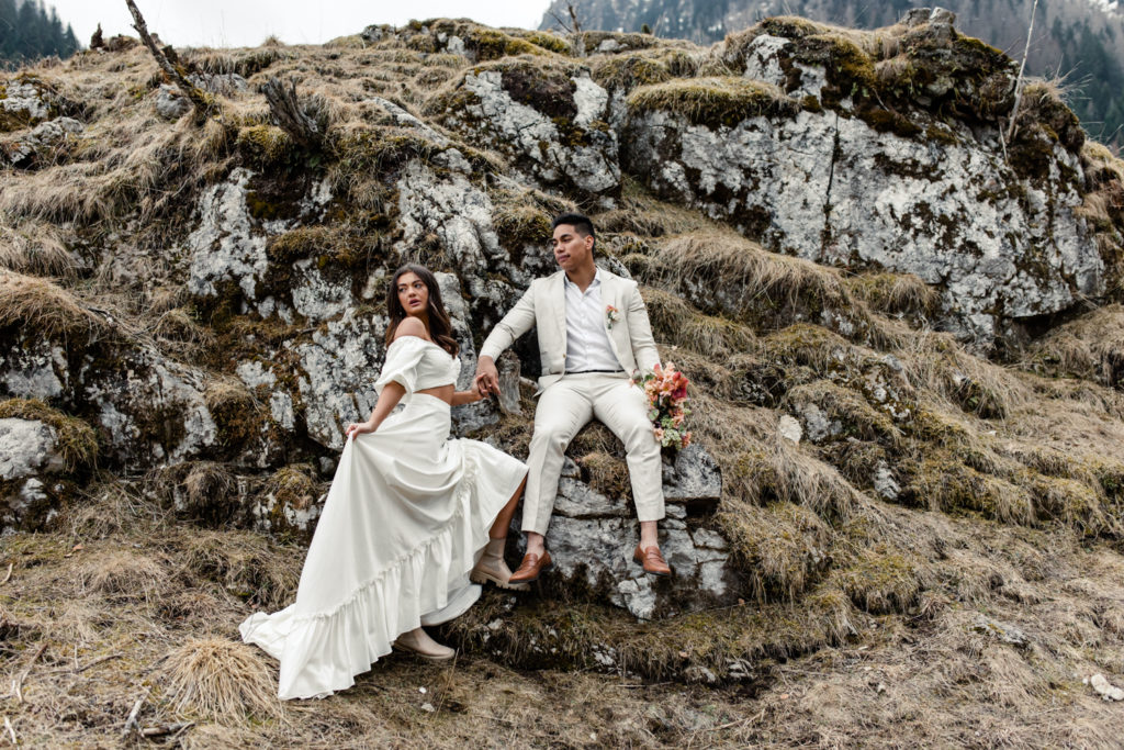 Groom, in cream suit, holding hands with bride, in white dress holding pink bouquet, on a mountain in Dolomites Italy. Photographed by Charlotte Wedding Photographer.