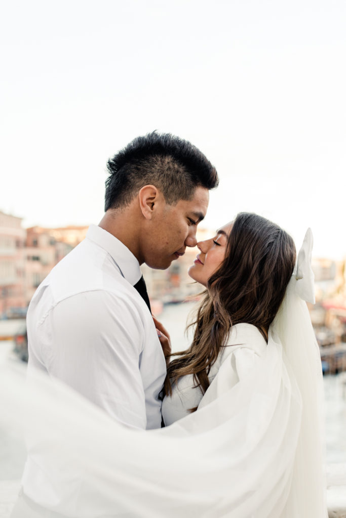 Bride, in white gown and veil, nose to nose with groom in Venice Italy. Photographed by Charlotte wedding photographer. 