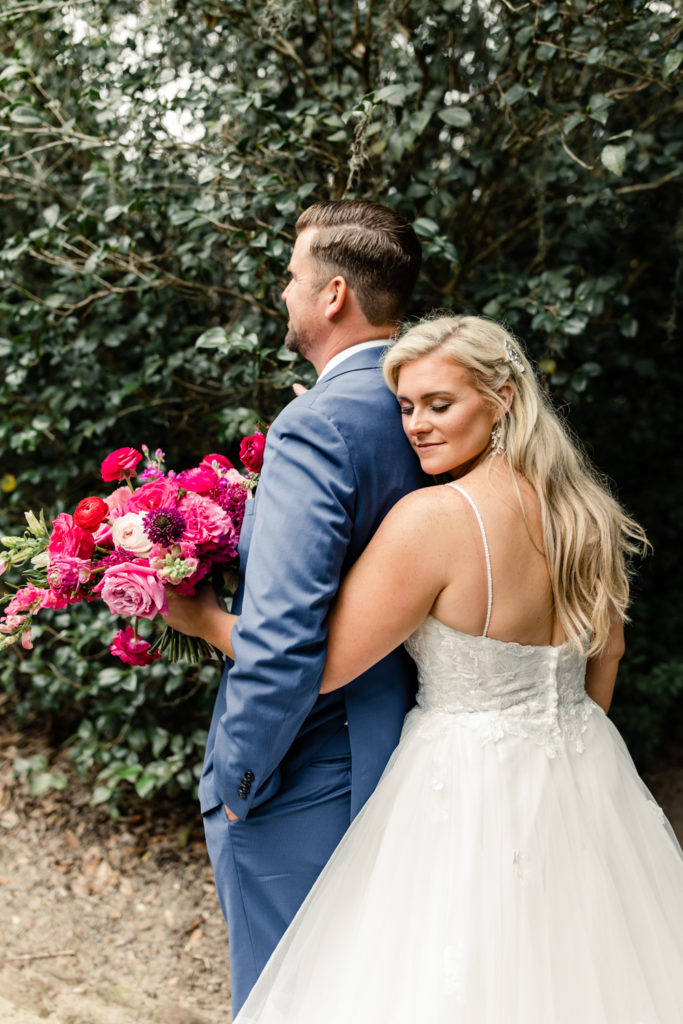 Bride, in white dress, holds pink bouquet while hugging her groom at Middleton Place wedding venue in Charleston. Photographed by Charlotte Wedding Photographer.