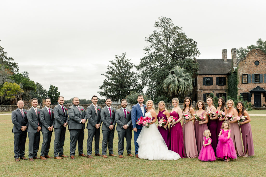 Bride and groom standing with their wedding party in grey suits and pink dresses at Middleton Place wedding venue in Charleston. Photographed by Charlotte Wedding Photographer.