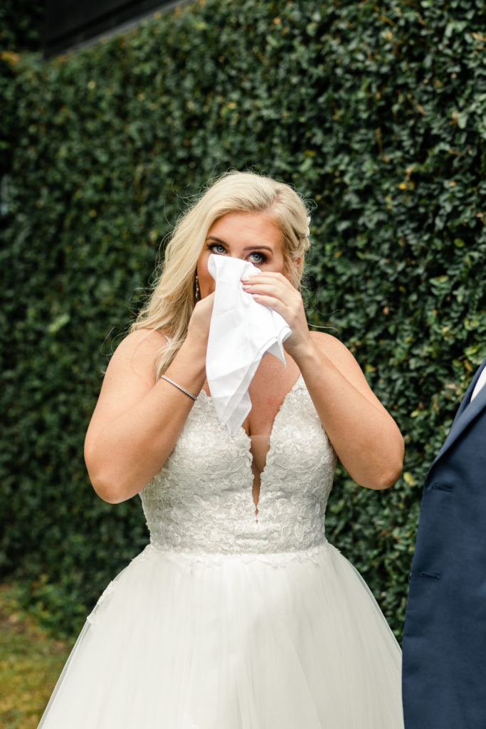 Bride, with blonde hair wearing a white dress, wipes her tears with a white handkerchief at the Middleton Place wedding venue in Charleston.