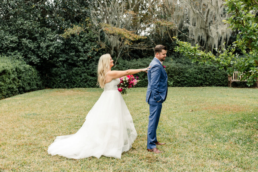 Bride, in white dress holding a pink bouquet, seeing her groom, in a blue suit, for the first time at Middleton Place wedding venue in Charleston. Photographed by Charlotte Wedding Photographer.