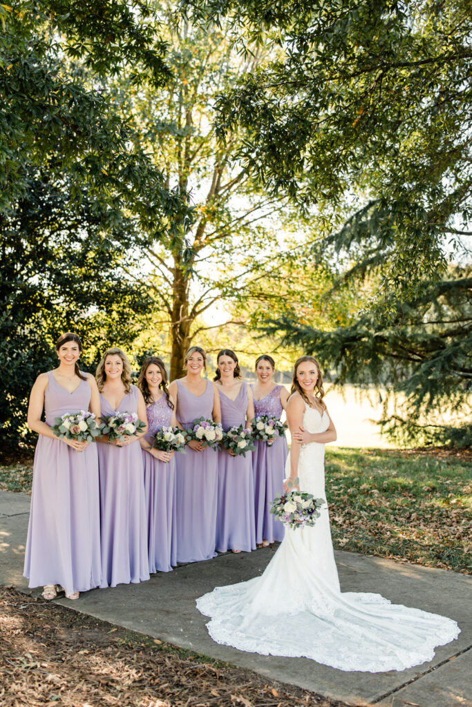 Bride, in white dress, standing with six bridesmaids in purple dress at Long View Country Club wedding venue in Charlotte NC