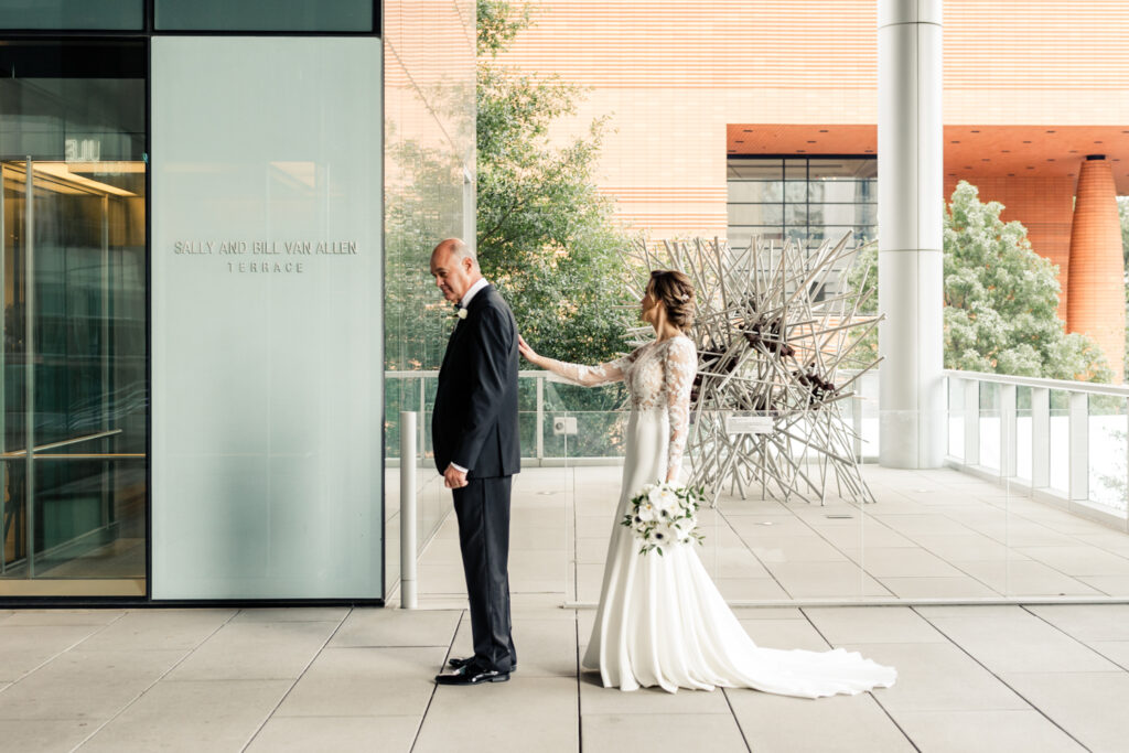 Bride, in white lace dress, seeing dad, in black suit, for the first time at the Mint Museum wedding venue in Uptown Charlotte