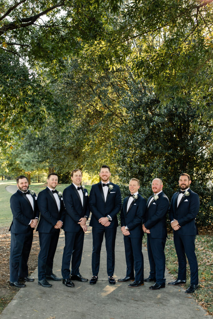 Groom and groomsmen dressed in navy suits and bowtie standing at Long View Country Club wedding venue in Charlotte NC