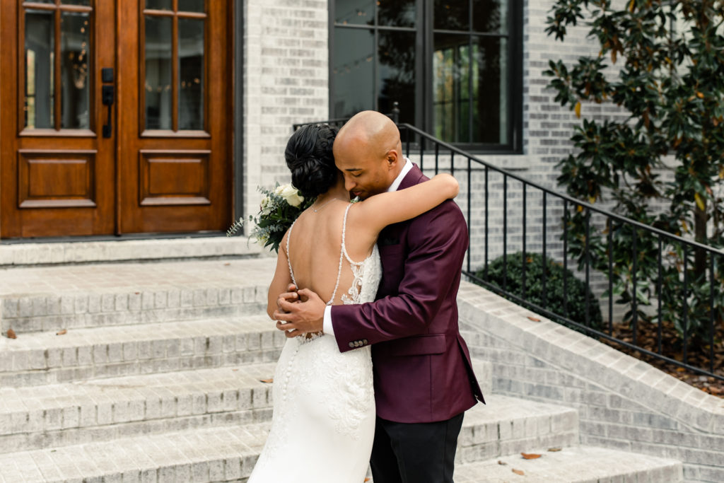 Bride, in white lace dress, hugging groom, in burgundy suit, for the first time at the Bradford wedding venue in Raleigh NC.