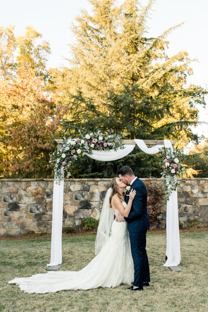 Bride, in white dress and veil, kissing groom, in navy suit, for the first time during ceremony at Long View Country Club wedding venue in Charlotte NC