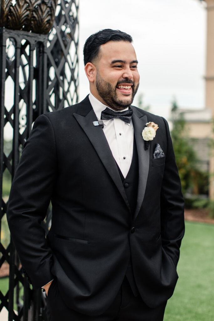 Groom, in black suite and bowtie, smiling as he watching his bride walk down the aisle at The Highlawn Wedding venue in New Jersey. Photographed by Charlotte Wedding photographer.