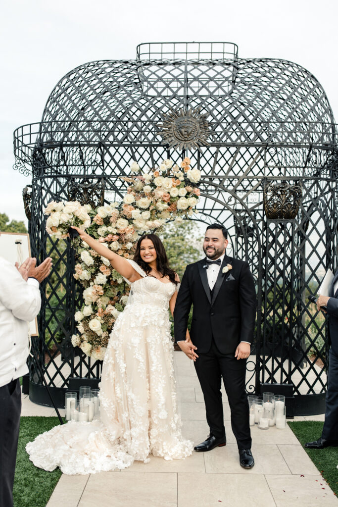 Bride, in white lace dress, holding hands with groom, in black suit, smiling at The Highlawn Wedding venue in New Jersey. Photographed by Charlotte Wedding photographer.