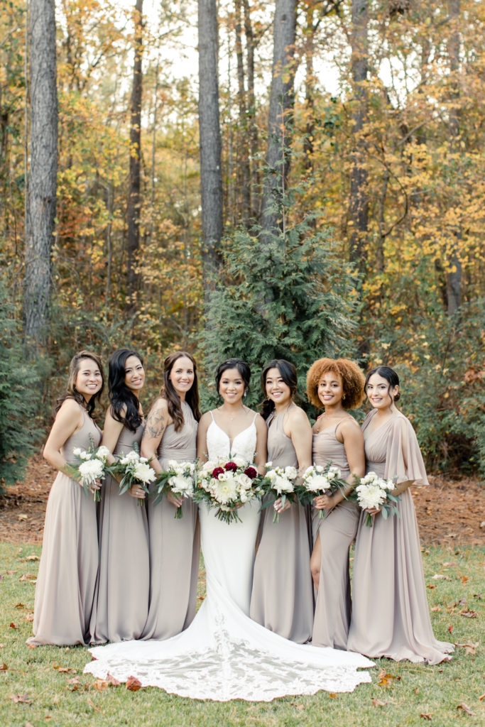 Bride, in white lace dress, standing with six bridesmaids, in cream dresses at the Bradford wedding venue in Raleigh NC.