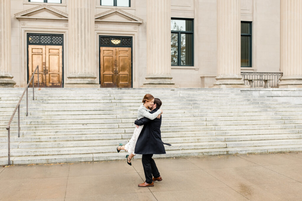 Groom spins his bride in front of tall stairs and gold doors. Photographed by Stephanie Bailey Photography. 