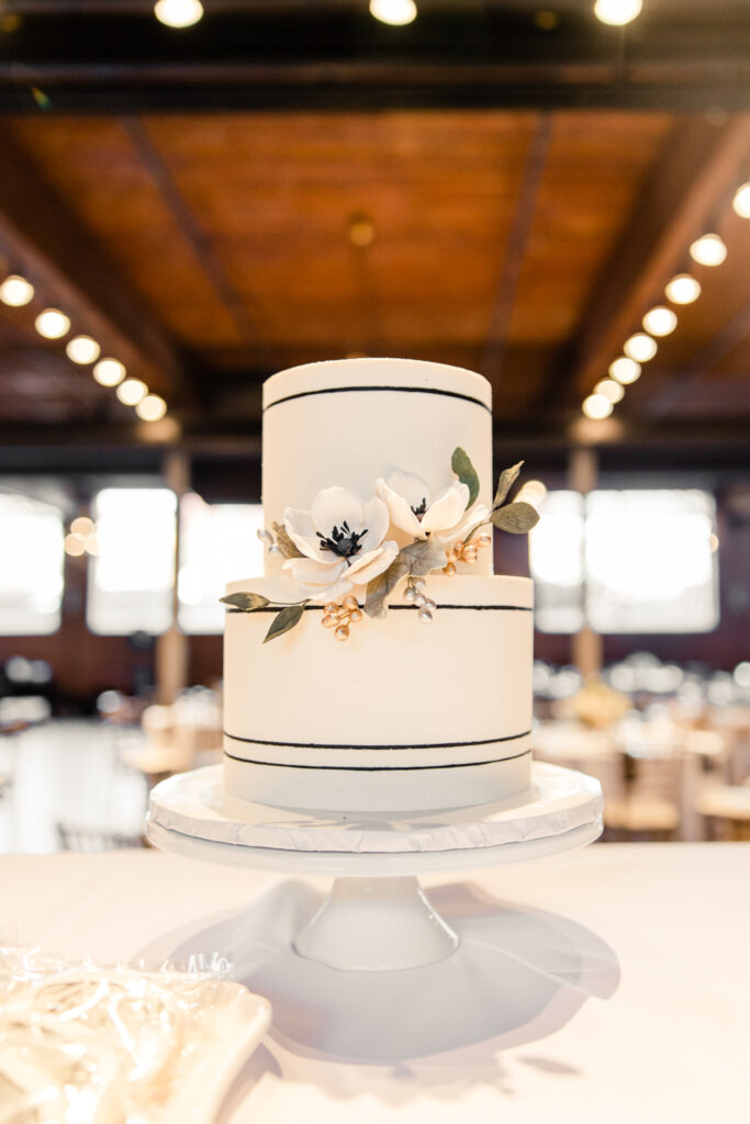 Two tiered white cake decorated with black stripes and white flowers at Byron's South End wedding venue. Photographed by Charlotte wedding photographer, Stephanie Bailey Photography.